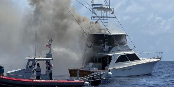 Boat with smoke coming off it from a fire and a coast guard boat