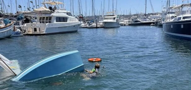 Sinking sailboat with sailor swiming twoard life preserver