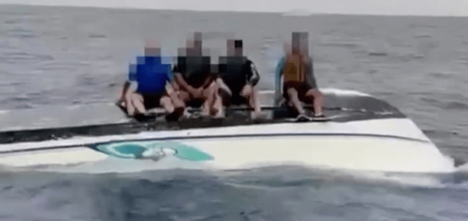 4 People sitting on a capsized boat.