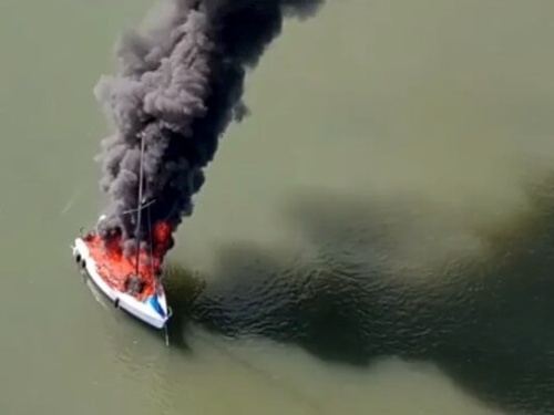 An aerial view of a boat on fire in the water.